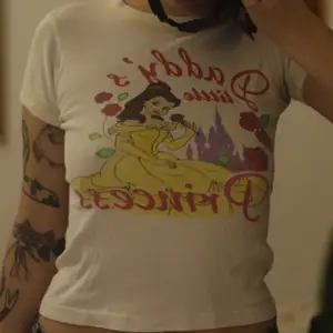 Vit t-shirt med tryck föreställande Belle från Skönheten och odjuret med texten ”Daddys little princess” 