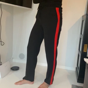 Svarta byxor med röda ränder - Ett par svarta sköna byxor i tunt tyg. Använda ett fåtal gånger. Mycket bra skick. 