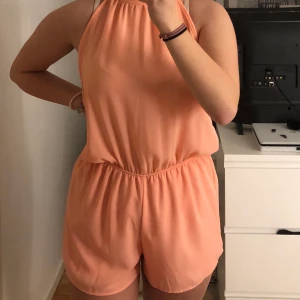 Jumpsuit från NLYONE - En persikofärgad jumpsuit från NLYONE i st S. Säljer för den inte är min stil längre. aldrig använd av mig, men fått av en kompis. Inga synliga skador. ärmar och band att knyta runt halsen, öppen rygg. Sömmar vid midjan. 