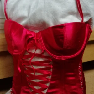 Snygg Korsett!  - Röd trendig korsett / korsettop i grövre sidenliknande material med riktigt bekväm stretch. Storlek är 75a men är större i sin storlek! Den passar utmärkt även till en stor b-kupa utan att ser dumt ut. Den har ett par insydda skenor så den stannar kvar på sin plats snyggt. Spänns i ryggen och passformen är som sagt flexibel, runt XS till liten M ungefär. Den är såklart hel och i väldigt bra skick. Sparsamt använd! Kommer från H&M och dem säljs inte längre. Se bilder. Fraktkostnad och fraktalternativ går att ändra efter önskemål. Säljes till fastpris. 