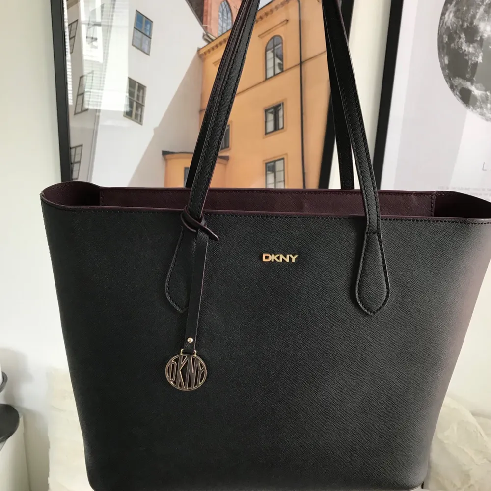 Äkta DKNY väska köpt i USA. Snygg svart väska med guldiga och vinröda detaljer. Dustbag kommer med. Mycket fint. Möts upp i Stockholm och fraktar (köparen står för frakten). Väskor.