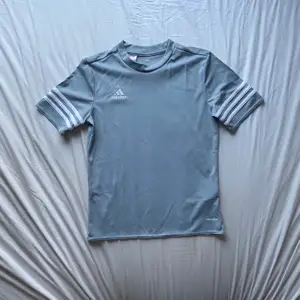 Blå-grå T-shirt i träningsmaterial från adidas. Nästan aldrig använd, nyskick. Storleken är ”youth size large”, skulle säga att den passar xs-s. Skriv om ni har fler frågor osv! Köpare står för frakt!