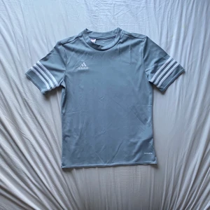 Adidas T-shirt  - Blå-grå T-shirt i träningsmaterial från adidas. Nästan aldrig använd, nyskick. Storleken är ”youth size large”, skulle säga att den passar xs-s. Skriv om ni har fler frågor osv! Köpare står för frakt!