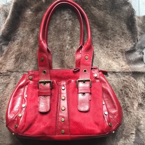 Coccinelle Handväska - Fin handväska som tyvärr aldrig kommit till användning. Helt ny, 100% äkta skinn/koskinn, nitar.  En mobilficka på insidan samt ett fack med blixtlås. Två robusta handtag. Nypris: ca 2600 kr  Inköpt från Yoox  Bredd ca 40cm Höjd  ca 24cm Djup 14cm