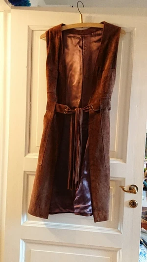 Lång läderväst med fransar - Längre väst i läder köpt på en mässa för några år sedan. Bältet har fransar. Skriv gärna till mig om du önskar flera foton! Köparen står för frakt om vi inte kan mötas upp i Stockholm.