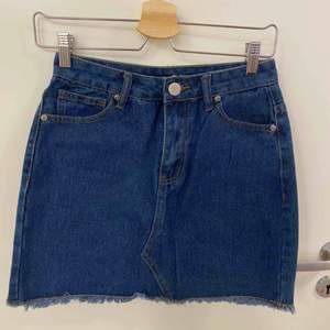 Jeans kjol med hällor upptill, fickor både fram och bak, fransar längst ner samt knapp o dragkedja som öppning. Aldrig använd 