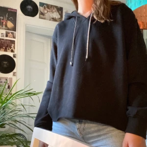 Svart hoodie med diamantsnören! - En supersnygg svart hoodie med fake diamanter som snöre, jag har croppat hoodien själv. Ganska simpel men diamanterna gör den lite extra! Från &Other Stories. Den är även jätteskön på insidan! Frakt tillkommer:)