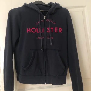 Hollister hoodie  - En marinblå Hollister hoodie med rosa detaljer. I storlek s men passar även dem som är xs. Köptes i en Hollister butik för 400kr. Använd några gånger men i ett väldigt bra skick. Säljer pågrund av att jag har för många hoodies. Köparen står för frakten💕