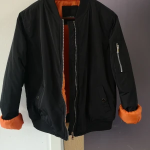 Tjockare bomberjacka svart/orange strl S - Säljer nu en fin svart bomberjacka med orange foder. Jackan är något tjockare och passar höst/vinter (beroende på hur kall vintern är förstås 😅) märke: golddigga, strl: UK 10, motsvarar strl 36/38. Sparsamt använd, hittar inga fel på jackan. Möjligen någon mindre fläck som går att tvätta/torka bort. Pris inkl frakt