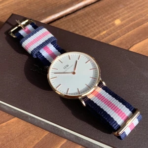 Daniel Wellington klocka - Den stora modell i roséguld med ett blå, vitt, rosa armband. Har inte använt så mycket och därför i väldigt bra skick💙🤍betala med Swish+köparen står för frakten