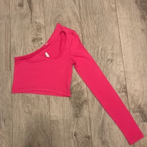 Rosa one shoulder topp - Rosa one shoulder topp med cut out vid nyckelbenet. Nyskick då den endast provats på. Storlek 36. Vid intresse kan eventuellt fler bilder skickas.