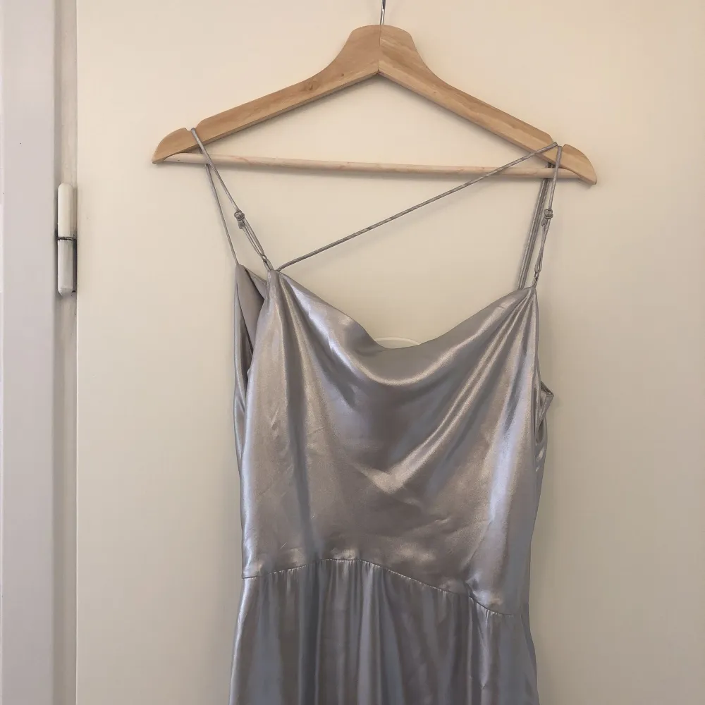 Assymetrisk klänning i silver från H&M. Aldrig använt. Markerad i midjan, slits i fram, justerbara axelband. Från H&M. Klänningar.