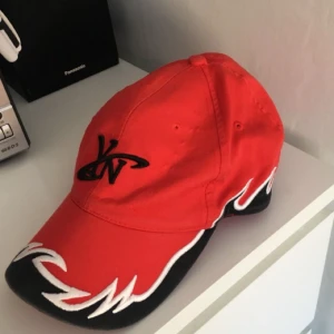  - Röd keps med tryck och detaljer. Justerbar storleksrem på baksidan. Använd en gång.