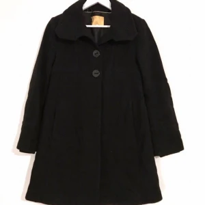 Svart kappa, 70% ull, XS - Svart kappa i 70% ull med mjukt foder inuti! Krage som går att fälla upp till polo. Två stora knappar längst upp, och dold knäppning nedåt. Muddar längst ned inuti ärmarna. Damkappa, vinterjacka.   Litet luddig på bilden då den legat med annat ylle och behöver slätas ut litet, men detta ordnas förstås inför sälj! 🌹  Kan mötas i Stockholm eller skicka mot fraktkostnad! ✨🌸✨ 