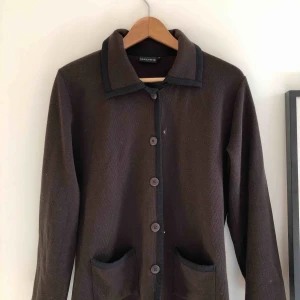  - Kofta med krage, knappar och fickor! Kan användas som tunn jacka under sommaren. Mörk brun med markerade kanter Storlek L men funkar till mindre, beroende på hur man önskar passformen