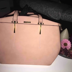  - En helt oanvänd handväska med färgen ljus rosa. Den är i jättebra skick och lätt att styla.  OBS! Eftersom den låg i en låda blev de lite färg av vanliga färgpennor där bak som går bort lätt