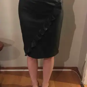 Svart kjol i läderimitation med en snygg volang framtill