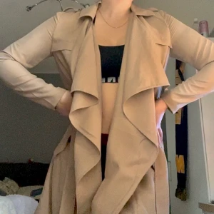 Tunn beige kappa - Skön vår kappa, jätte fint skick och skönt material! Ganska tunn så går att använda under en tjockare jacka!