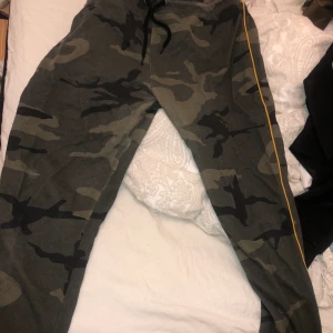 Kamouflage mjukisbyxor strl XL - Snygga och bekväma mjukis byxor som är använda mindre än 10 gånger. Dem är inte stretchiga men passar perfekt om du tex har strl L som jag och gillar att ha dem lite baggy. En gulrand på vadera sida av benen. Nypris 200kr. Mitt pris 50kr+ eventuell frakt 