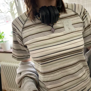 Babytee  - Babytee/barntröja passar S/Xs och M. Gråa och bruna ränder med ett R på vänstra bröstet. Frakt ingår inte🐱😝