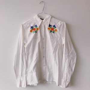 Bomullsskjorta med brodyr  - Superfin skjorta i 100% bomull med blom-brodyr på bröst och bak. Inköpt i liten butik i Italien men har tyvärr aldrig kommit till användning. 