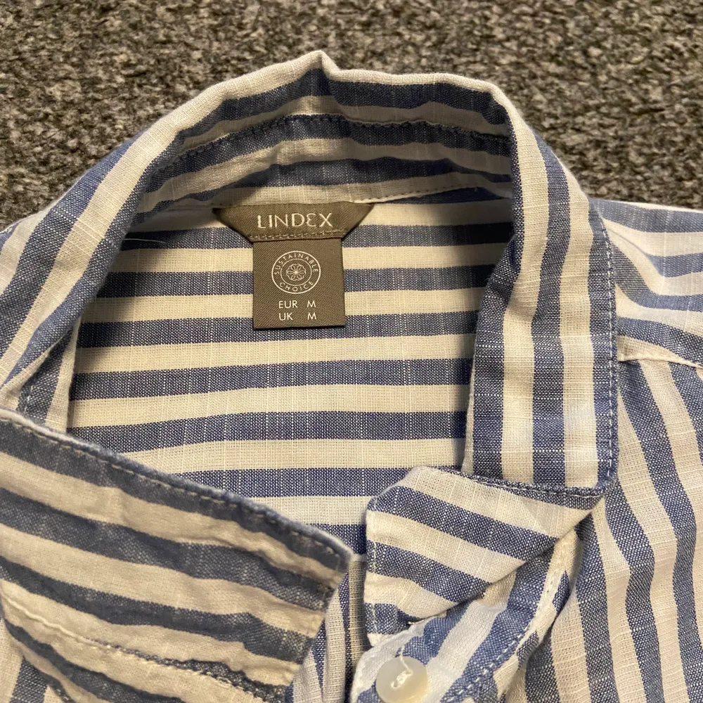 En fin skjorta från Lindex med ljusblåa ränder. Enbart använd någon enstaka gång och är därför som i nytt skick. Säljer för att den bara hängt i garderoben och aldrig kommer till användning. Nypris: 399kr. Köparen står för frakt. . Skjortor.
