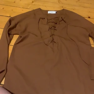 blus från Na-kd  - blus med snörning och vida armar. brun i detta ljus men i verkligheten är den mer rosa/röd/brun