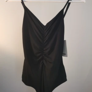 Oanvänd body med scrunch - Fin oanvänd body med knäppning i grenen och justerbara axelband. Har scrunchdetaljer fram och bak. Jag har oftast S men denna XS passar bra. Köparen står för frakten. 
