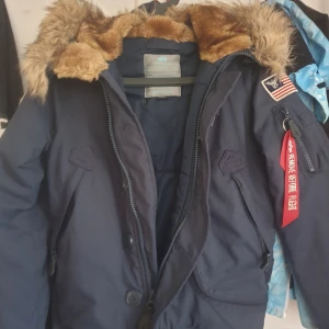 Alpha Industries  vinter jacka - Snygg jacka med massa fina detaljer från Alpha Industries. - Luva med avtagbar fuskpäls - Stängs med dragkedja och knappar - Femficksmodell arav en invändig - Ribbstickad mudd ärmslut och nederkant- - Fodrad