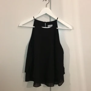 Svart topp XS  - Svart, festlig topp med diskret volang nedtill. Nyskick. 100% polyester. 