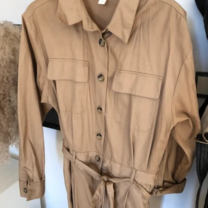H&M cargojumpsuit beige - En beige jumpsuit med långa ben och armar från H&M, tillhörande snöre att knyta i midjan och bruna knappar upptil, även dragkedjan nedtill under knapparna för bättre passform! I väldigt bra skick! Passar mig som har storlek S/M och är 170 cm lång.