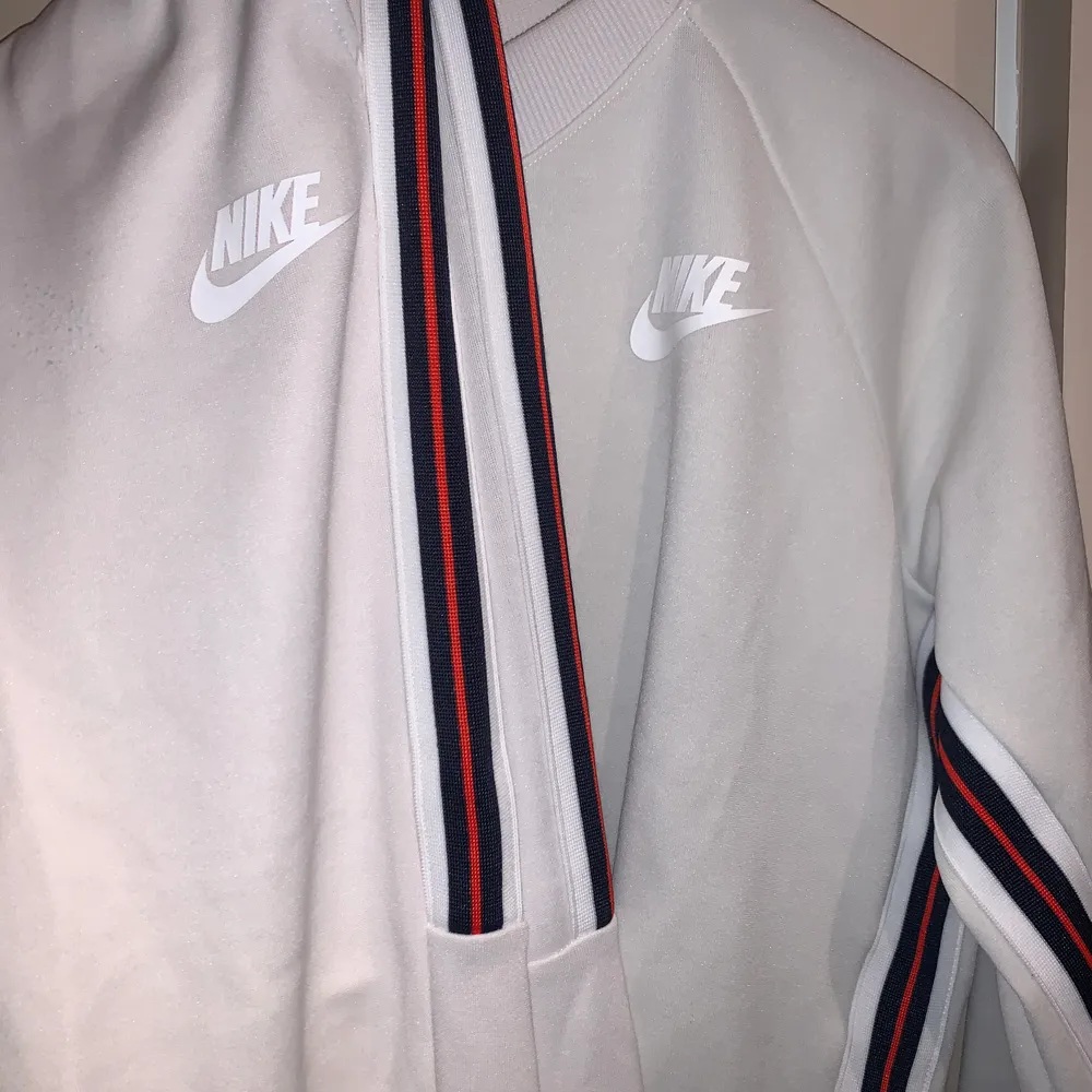 En benvit Nike tracksuit med revär på sidan. Nypris tröja 399kr byxa 579kr. Setpris 350kr + frakt. Hoodies.