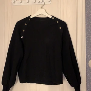 Svart Tröja med Detaljer - En svart tröja med 5 ”knappar” på båda sidor. Tröjan kommer från Mango och är nästintill oanvänd. Nypris: 299kr. Kan frakta men då står köparen för den kostanden!
