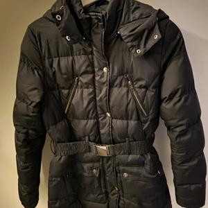 Svart vinterjacka med midjebälte strl S - En vinterjacka från cubus med några år på nacken men fortfarande i väldigt fint skick! Den går just under rumpan på mig som är 158 cm lång och är riktigt snygg på. Bild gör den inte rättvisa. Passar en S-M