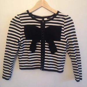  - Svartvit randig finstickad kofta med stor svart rosett från HM Divided, Storlek 34, 72% Viscose 27% Polyester 1% Elastan. Bra kvalité och i väldigt bra skick. Använd vid endast två tillfällen!