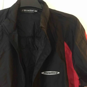  - Vindjacka / Träningsjacka från Newline i svart med röda detaljer. Reflexrand bak. 📬 Frakt 55 kr.