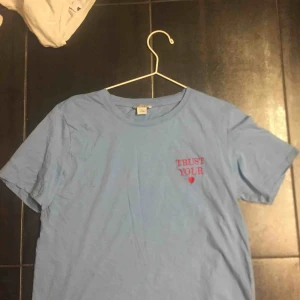  - Blå T-shirt med texten ”trust your ❤️” i rött, köpt på monki för ett tag sen