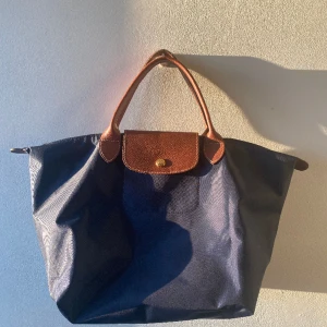 LONGCHAMP LE PILAGE - LONGCHAMP VÄSKA MÖRKBLÅ Väskan är i storleken ”onesize” och beställdes på hemsidan miinto för 1199kr💙Väskan är äkta och är oanvänd. Den har kortare handtag, jag vart inte nöjd med storleken, därför säljer jag den🤍🥂 Pris kan diskuteras☺️ dm för frågor