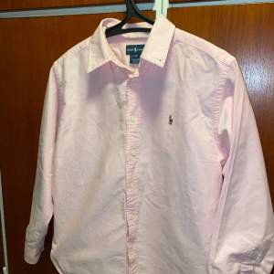 Säljer min rosa Ralph Lauren skjorta då då jag vuxit ur den. Den är ganska väl använd och i gott skick, men saknar den vänstra knappen till kragen. Annars inga märken eller skador vad jag kan hitta. Skjortan passar på dig som är 155-165. 