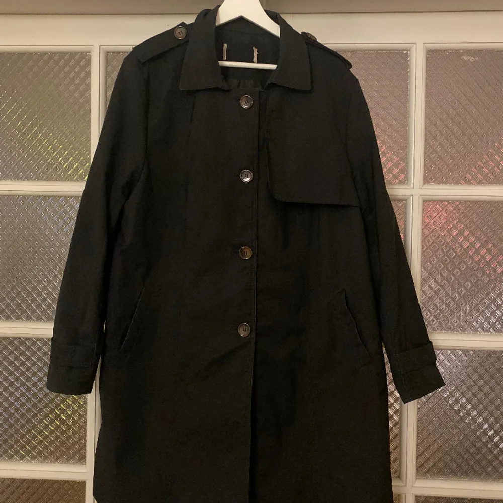 En fin svart kappa/trenchcoat med bruna knappar och coola detaljer. Storleken skulle jag uppskatta till en L. Köpt secondhand, men har inga tecken på användning.. Jackor.