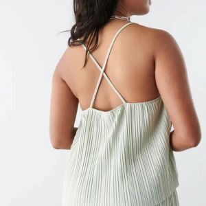 Plisserat linne - Plisserat linne med tunna axelband som korsas i ryggen. Linnet är grönt och har rynkade detaljer vid halsringningen.  Storlek: S  (Stor i storleken)