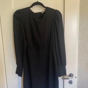 Svart långärmad klänning - Säljer en svart långärmad klänning. Den har en enkel men stilren design med en rund hals och långa puffärmar. Perfekt för höst- och vinterfester eller andra formella tillfällen. Klänningen är i nyskick och har en normal passform.