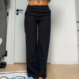 Svarta kostymbyxor med ränder - Säljer ett par snygga svarta kostymbyxor med diskreta ränder. Byxorna är midwaist och har en straight fit men går ut lite längst ner. De är i bra skick 