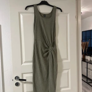 Grön ribbad klänning - En grön ribbad klänning med knytning framtill. Klänningen är ärmlös och har en normal passform.