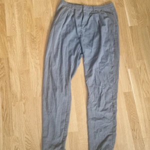 Grå kostymbyxor  - Grå kostymbyxor från Bik Bok. Fickor fram, 1 liten ficka baktill med knapp, dragkedja och spänne. Size L. Katt i hemmet.