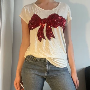 T-shirt med rosett - Vit T-shirt med röd rosett av paljetter. Lappen bortklippt men passar ca storlek xs-m. Möts på söder eller fraktar. Skriv innan ni trycker köp nu då jag är borta en del i sommar. 