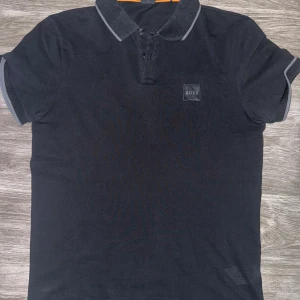 Boss Pike - I mycket bra skick och har klassisk design med krage och knäppning framtill. Perfekt för både vardagsbruk och mer avslappnade evenemang. Materialet är mjukt och bekvämt, vilket gör den idealisk för sommarbruk. Använts fåtal gånger ser ut som ny.