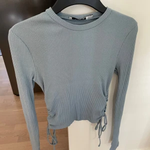 Långärmad topp med detaljer - Kan spännas till i midjan på båda sidor. Använd 1 gång