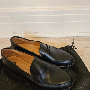 Penny Loafers från Hope - I svart läder, från Hope och i strl 41. Använda utomhus en gång. Har fått en gummisula från Vibram utanpå lädersulan, vilket kostade 500 kr hos skomakaren. Normala i passformen. Nypris knappt 4000 kr.
