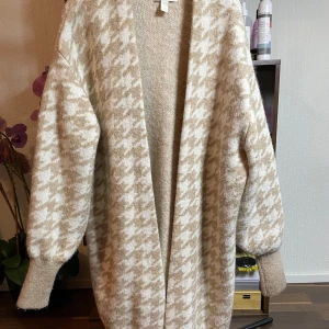Lång stickad kofta  - Lång Stickaf kofta ifrån HM beige och vit super skön att ha på sig under kalla tider inget användning på koftan 